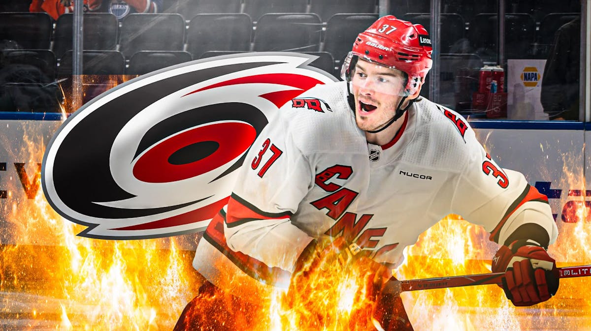 Andrei Svechnikov in middle of image looking happy with fire around him, Carolina Hurricanes logo, hockey rink in background