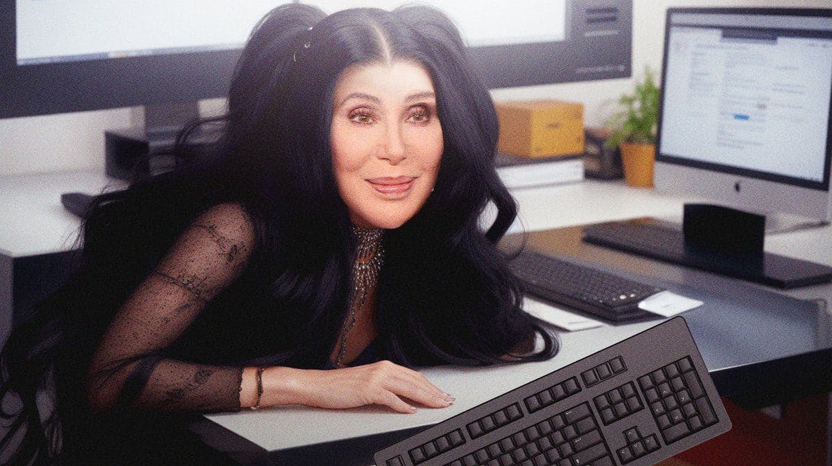 Cher at a computer with a keyboard in front of her.