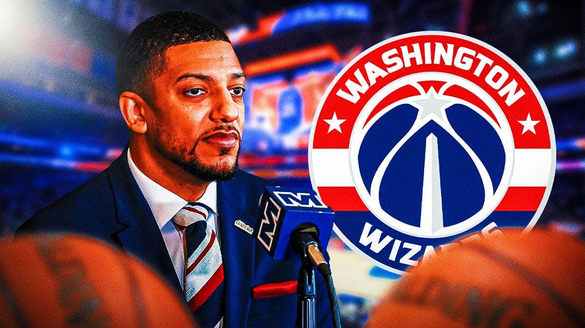 Wizards GM Will Dawkins frowns and looks sad next to Wizards logo