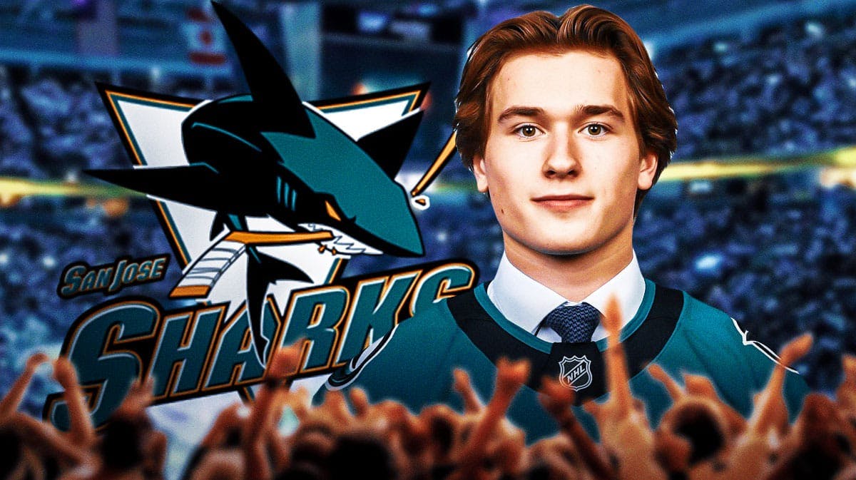 Macklin Celebrini in middle looking happy, San Jose Sharks logo, hockey rink in background