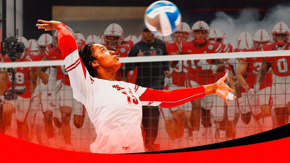 A player on the Nebraska volleyball team spiking over a net with the Nebraska football team in the background