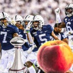 Penn State football players in the background, while in the foreground a peach along with a football trophy.