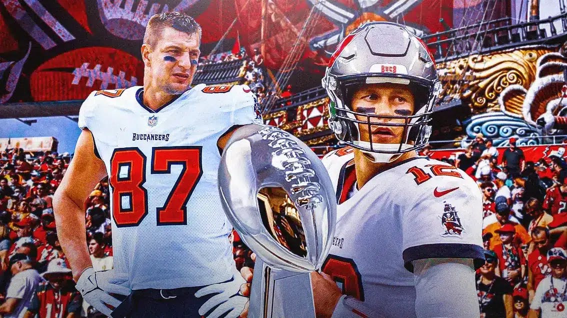 Buccaneers players Rob Gronkowski and Tom Brady in foreground, fans in background. Super Bowl trophy in center.