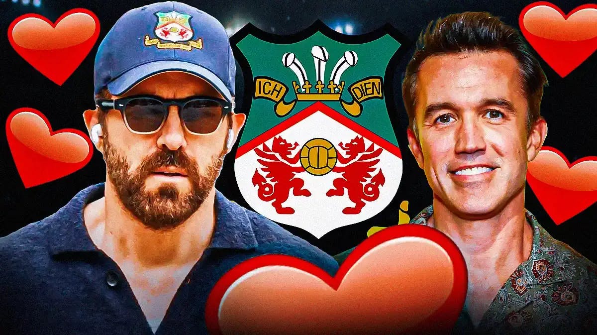 Ryan Reynolds & Rob McElhenney laughing in front of the Wrexham logo, heart emojis in the air