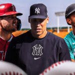 Aaron Judge in middle, Mike Trout and Julio Rodriguez on either side, baseball field in background