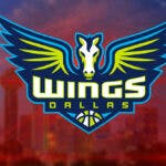 The WNBA Dallas Wings logo, in front of the downtown skyline of the city of Dallas, Texas
