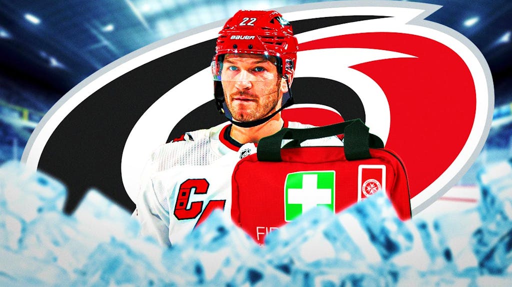 Brett Pesce in middle of image looking stern, first aid kit, Carolina Hurricanes logo, hockey rink in background