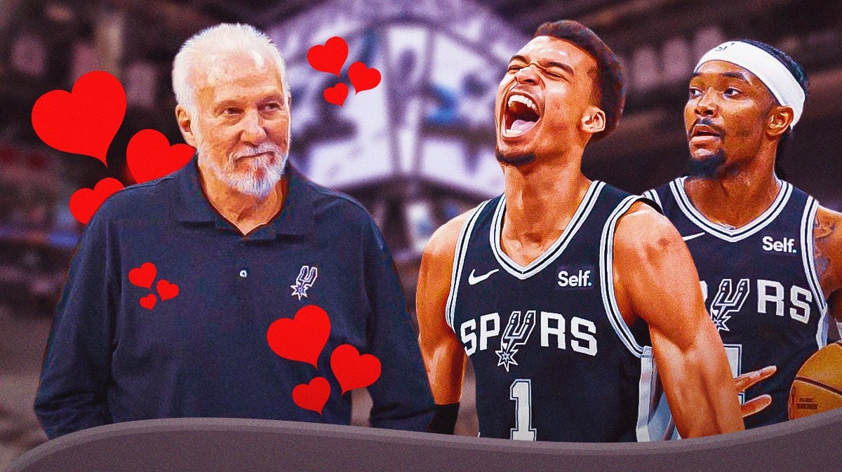 Spurs' Gregg Popovich with hearts all over him while smiling at Victor Wembanyama and Devonte' Graham